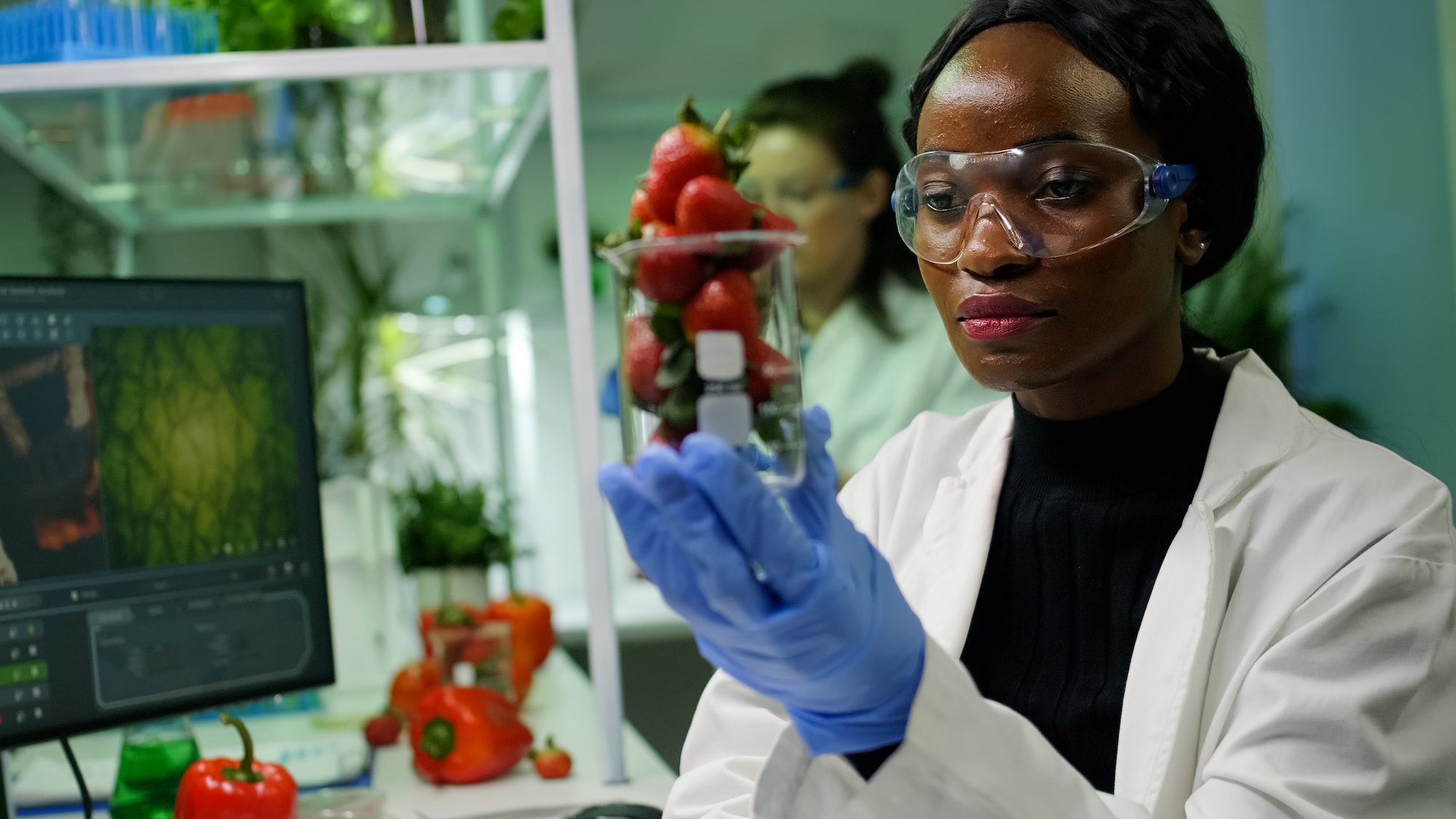 African researcher holding glas with strawberry injected with pesticides