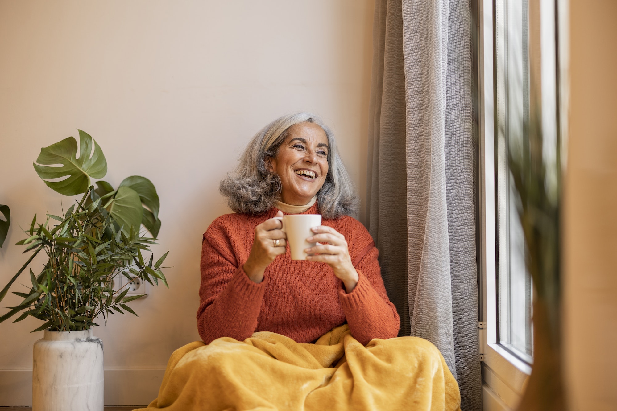 Portrait happy healthy older senior woman sitting at home and drinking coffee. next to the window.